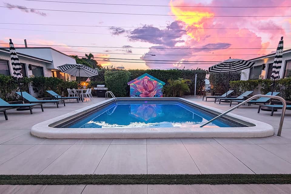 Resort pool at sunset with striped umbrellas, loungers, and colorful art installation backdrop