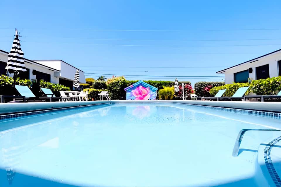 Bright turquoise swimming pool with colorful art installation, palm trees, and modern resort buildings