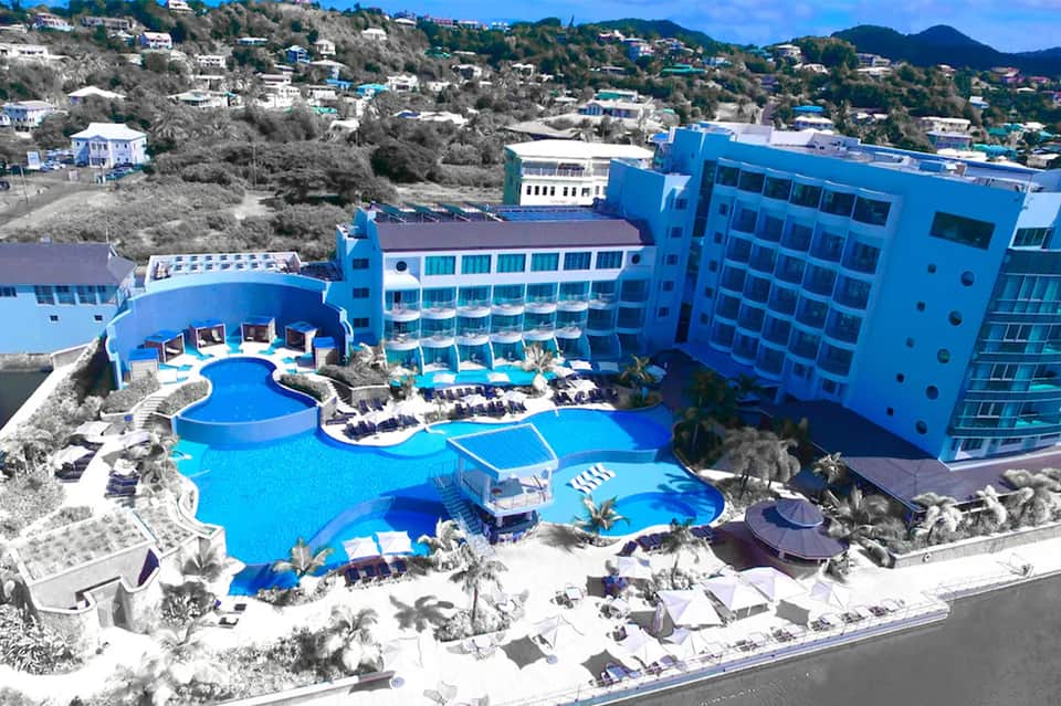 Aerial view of resort with bright blue buildings, curved swimming pools, and white sandy beach area