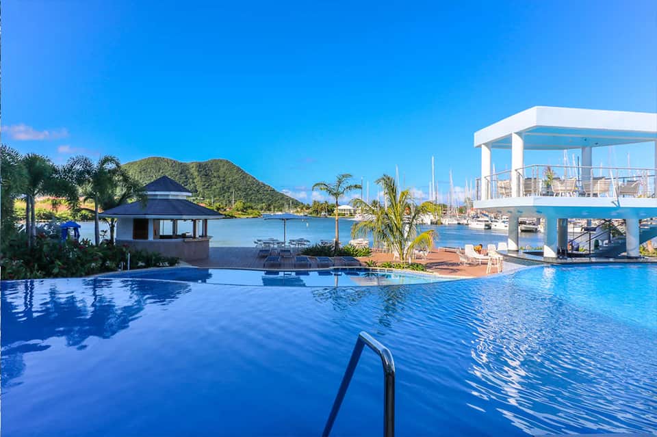 Resort infinity pool overlooking marina with sailboats and palm trees under clear blue sky