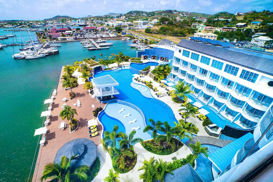Luxury resort with curved blue pools, palm trees, and sailboats in turquoise harbor bay