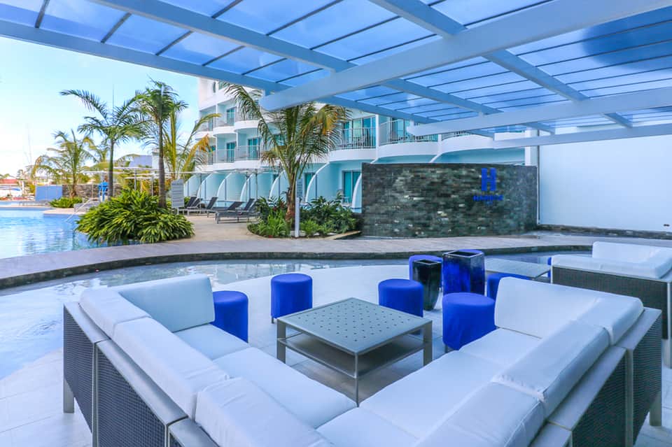 Indoor pool lounge with modern white seating, blue accents, and palm tree landscaping