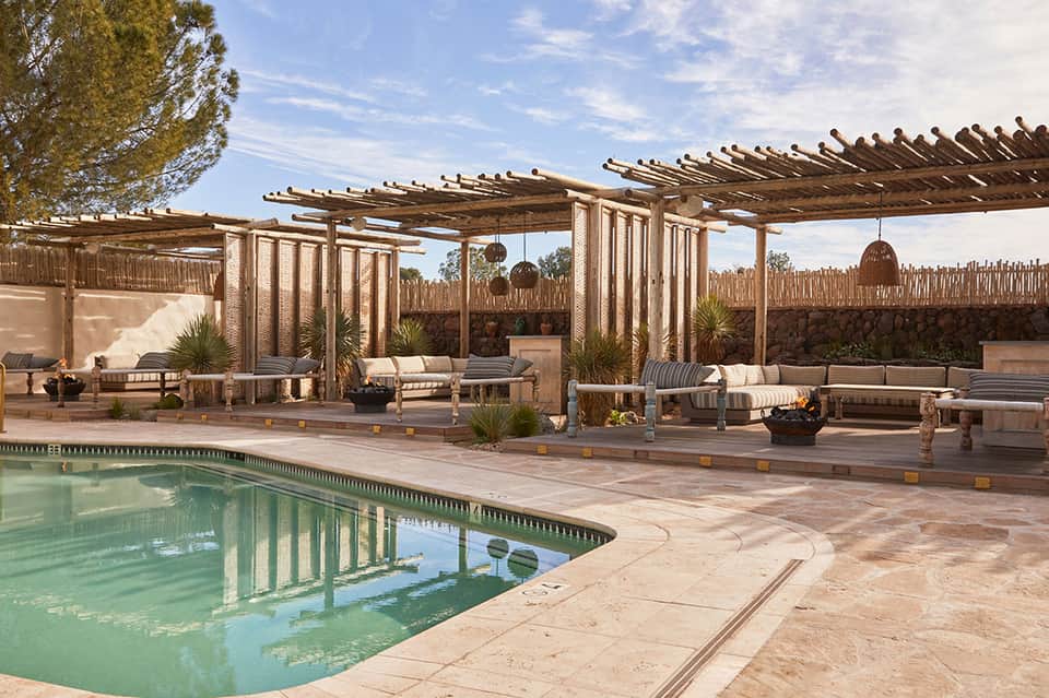 Desert resort pool deck with wooden pergolas, lounge seating, and clay-colored walls