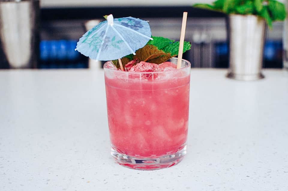Pink cocktail with blue umbrella and mint garnish on outdoor patio table