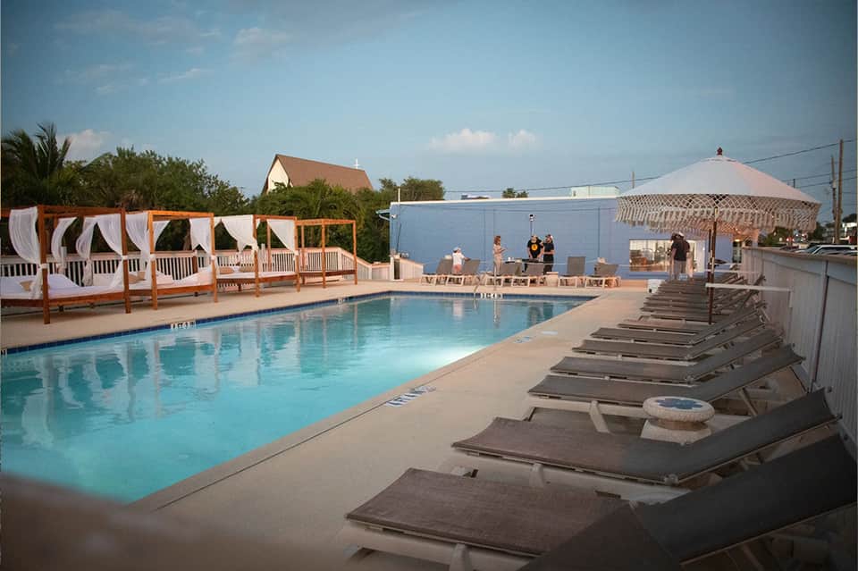 Resort pool with cabanas, lounge chairs, umbrellas, and waterfront setting at dusk