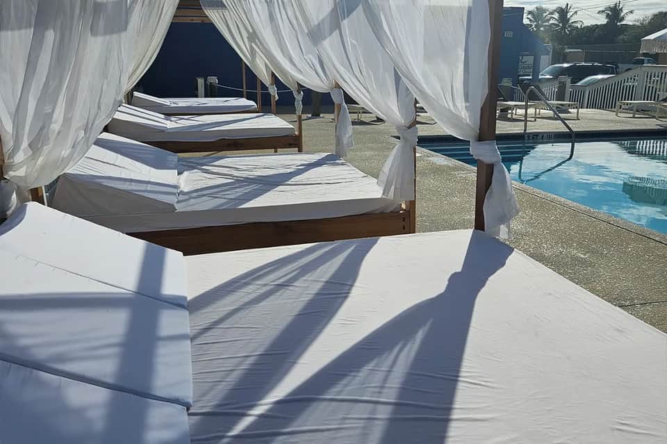 Cabana beds with white sheer curtains next to turquoise swimming pool