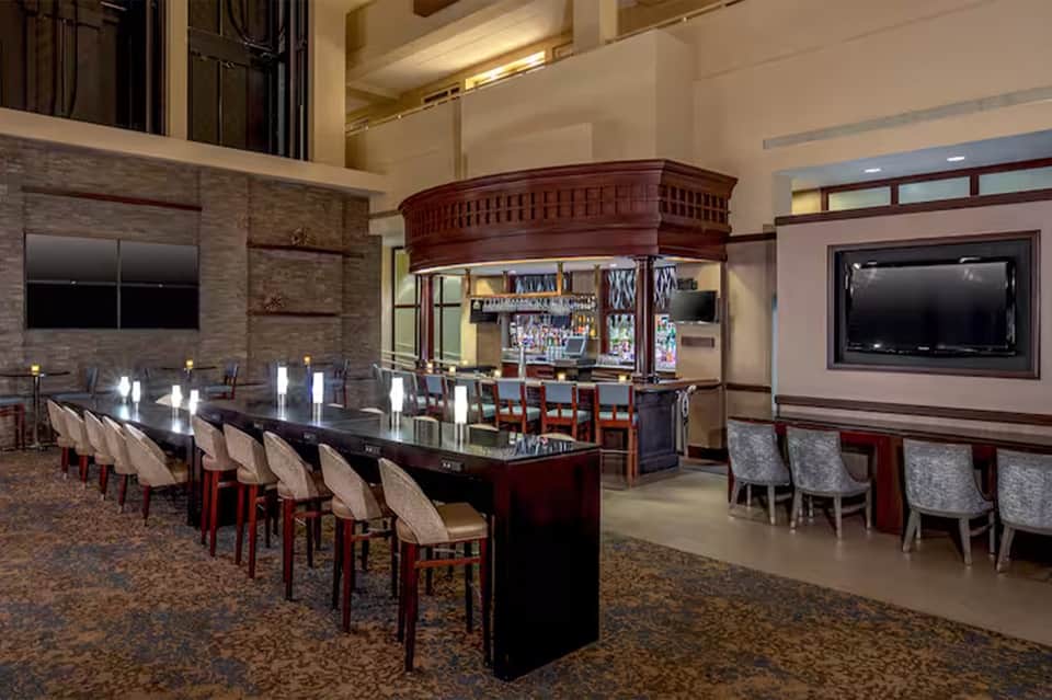 Grand bar lounge with dark wood bar, seating, high ceiling, and ambient lighting