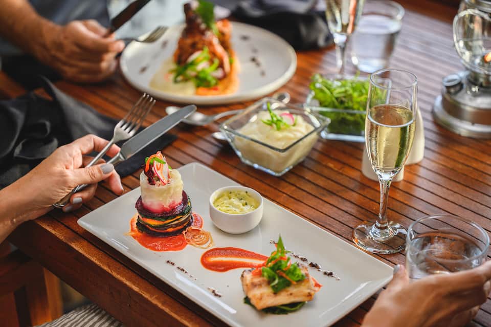Fine dining table with plated cuisine, champagne glasses, and decorative herb garnishes on wooden surface