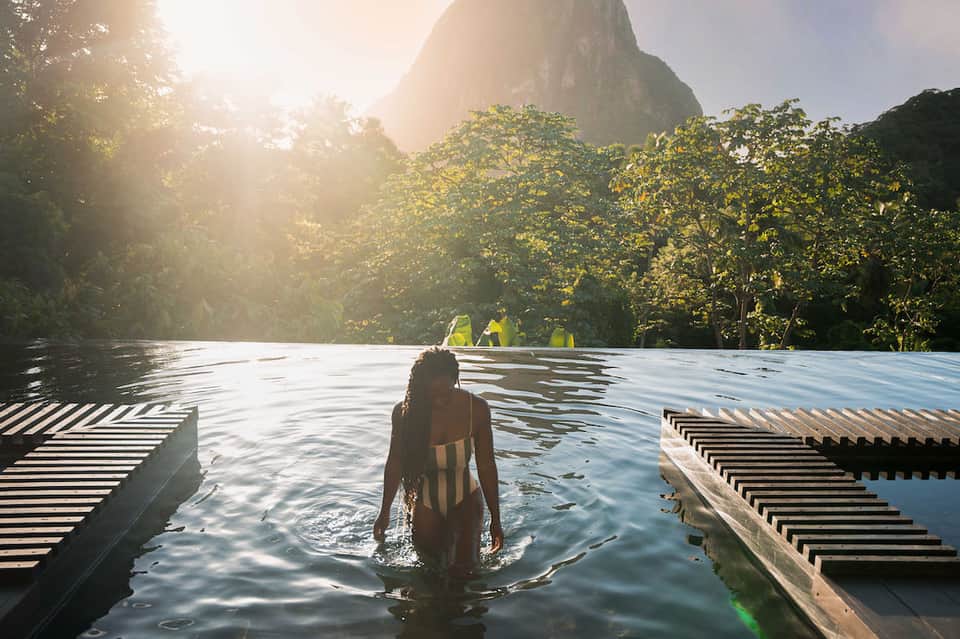 Woman swimming in natural hot spring pool surrounded by dense green vegetation and dramatic mountain cliff