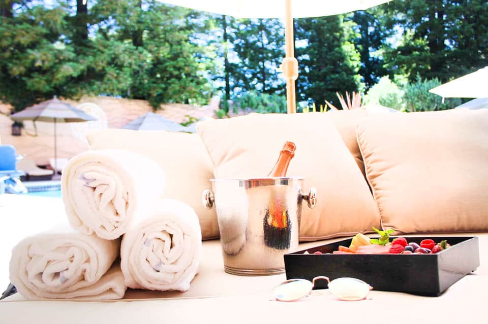 Poolside spa setup with rolled white towels, champagne bottle in ice bucket, and spa essentials on marble table