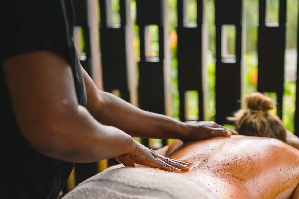 Exfoliation spa treatment applied to client's back outdoors in tropical setting