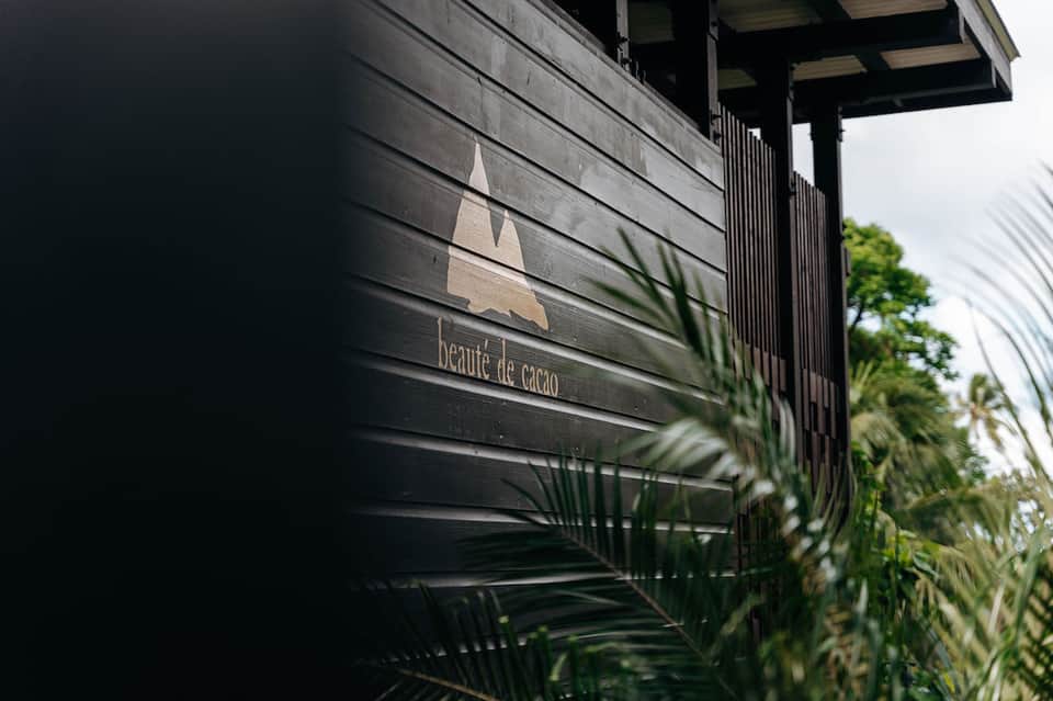 Modern spa entrance with dark horizontal siding and "Beauté de Cacao" signage surrounded by plants