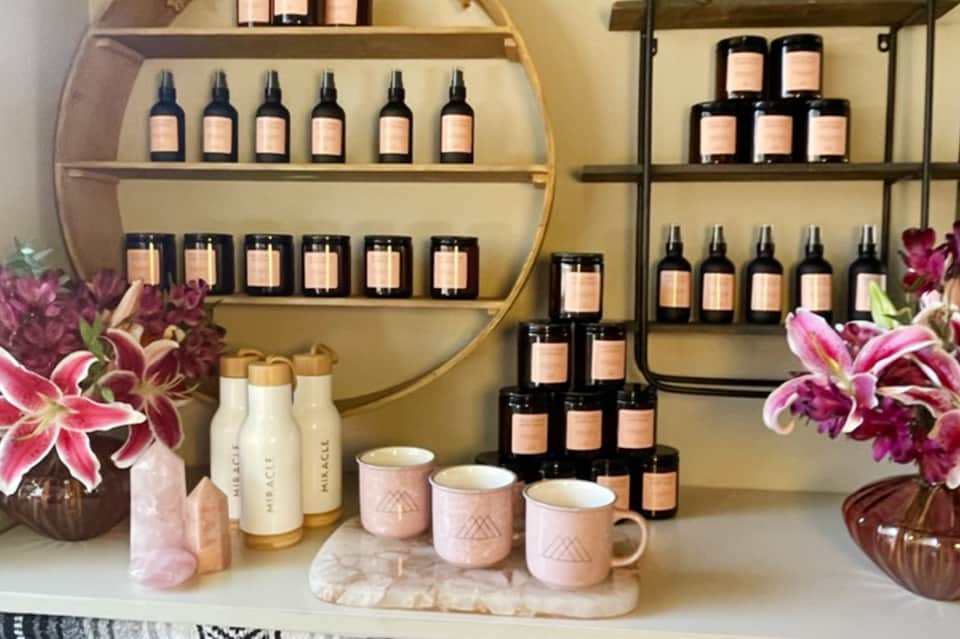 Spa retail display with black glass bottles, pink ceramic vessels, and fresh flowers on shelves