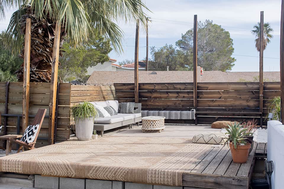 Wooden deck lounge area with white daybed, privacy screens, and palm trees