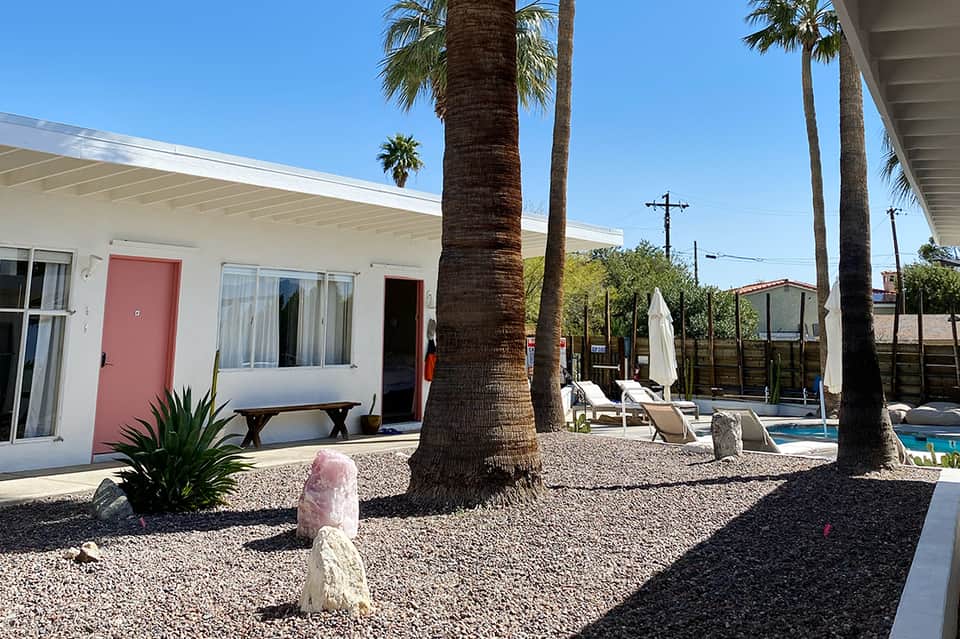 Retro motel with white building, palm trees, and pool area under clear blue sky