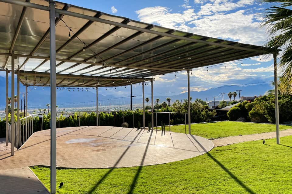 Contemporary wooden deck with glass pergola shade structure overlooking green lawn and scenic valley