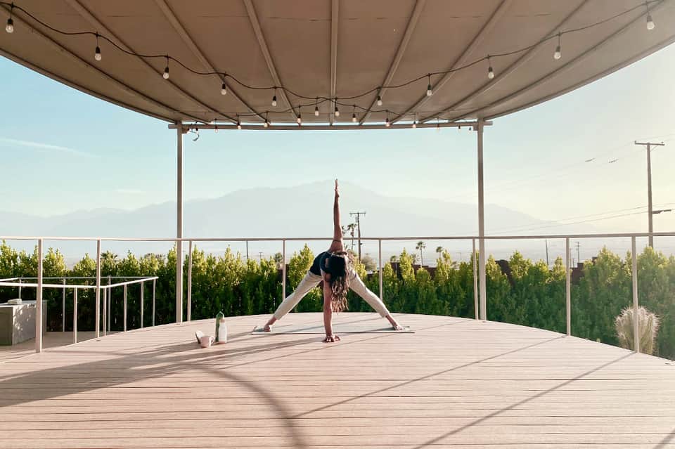 Woman doing yoga on wooden deck under retractable shade with mountain views in background
