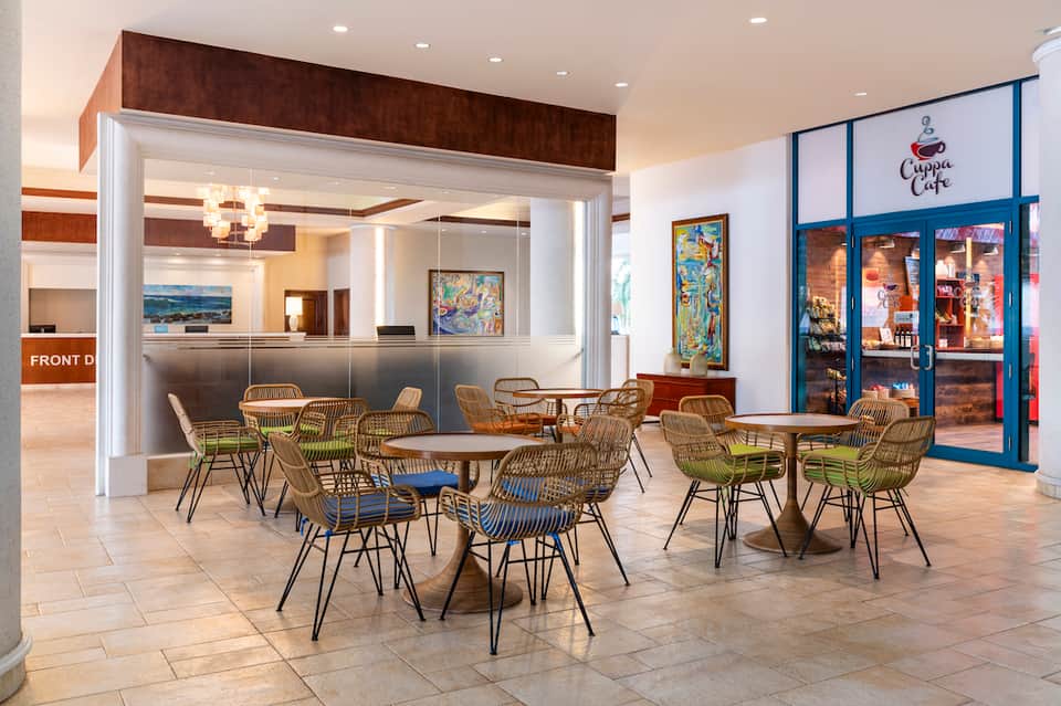 Modern hotel lobby café with woven chairs, round tables, and reception desk