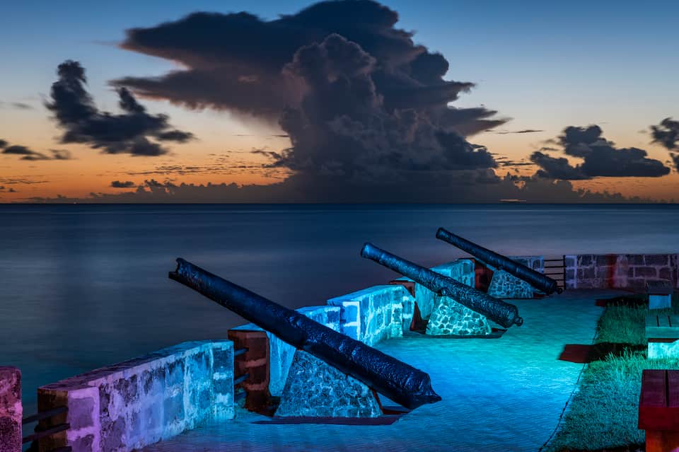 Abandoned boats illuminated with blue and purple lights at dusk over calm ocean water