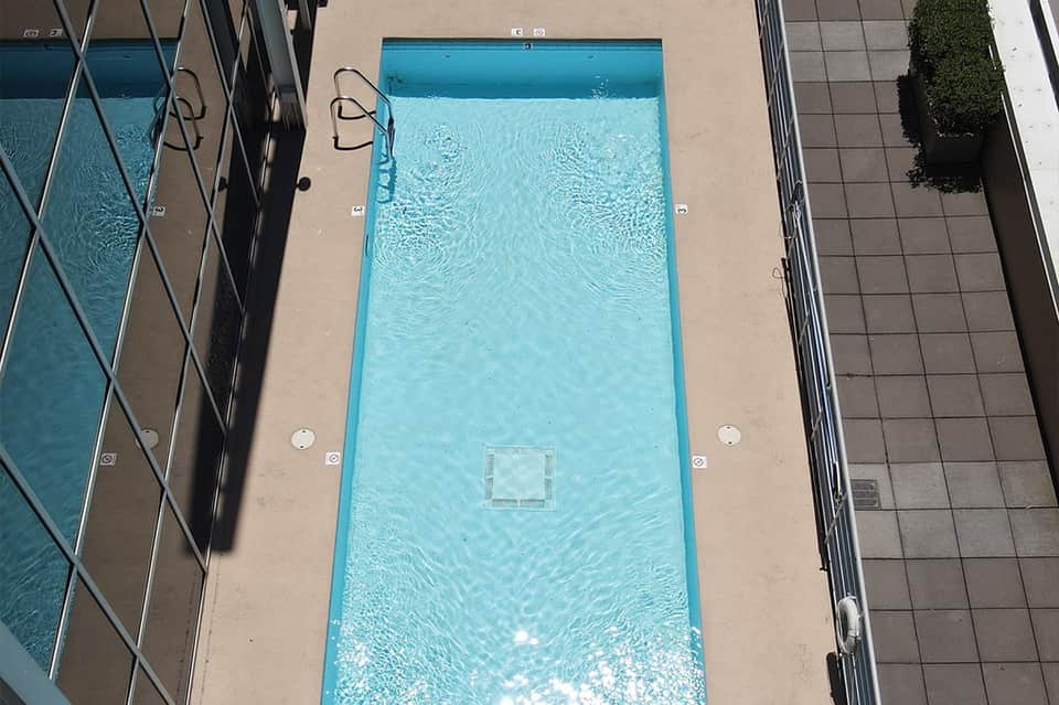 Aerial view of rectangular swimming pool with concrete deck and lounge chairs surrounding it