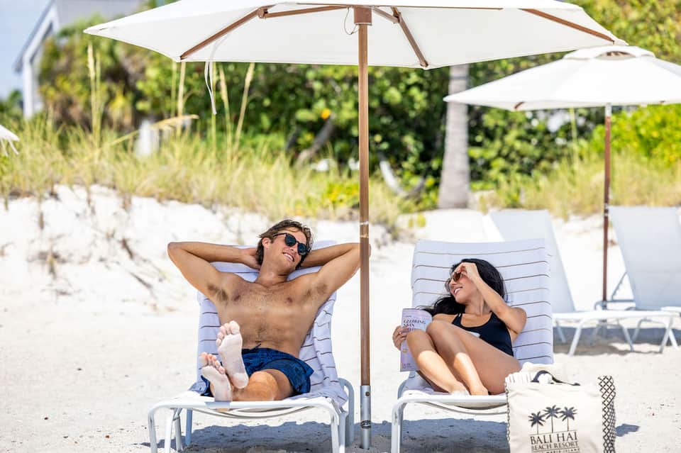 Couple lounging under white umbrellas on a sandy beach with palm trees in background