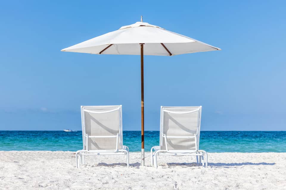 Two white lounge chairs under a white umbrella on a sandy beach with turquoise ocean