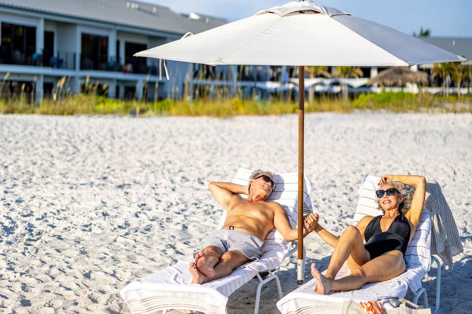 Couple relaxing on beach loungers under white umbrella with ocean view