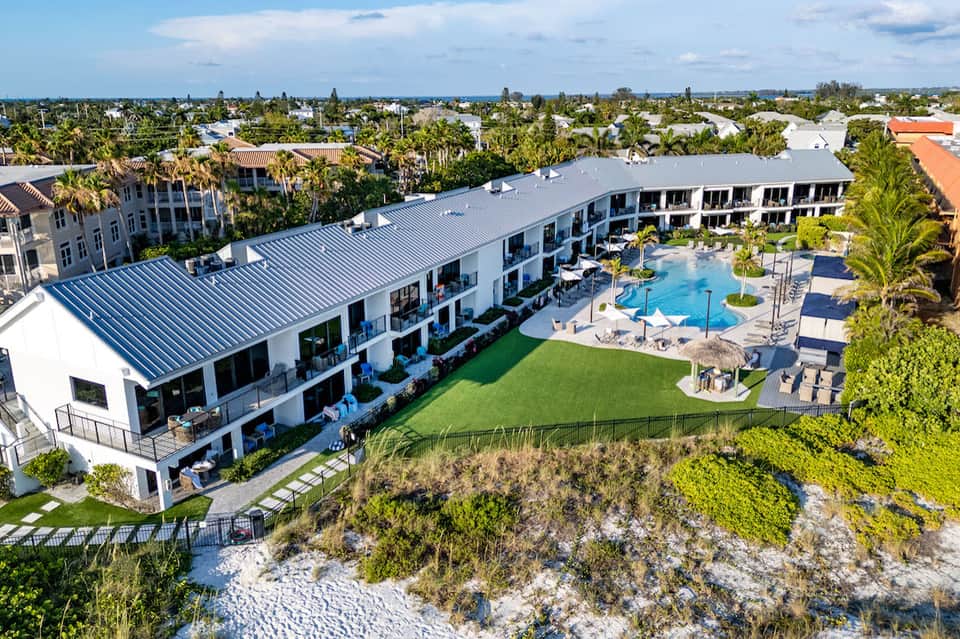Aerial view of modern waterfront resort with pool, lawn, and coastal dunes