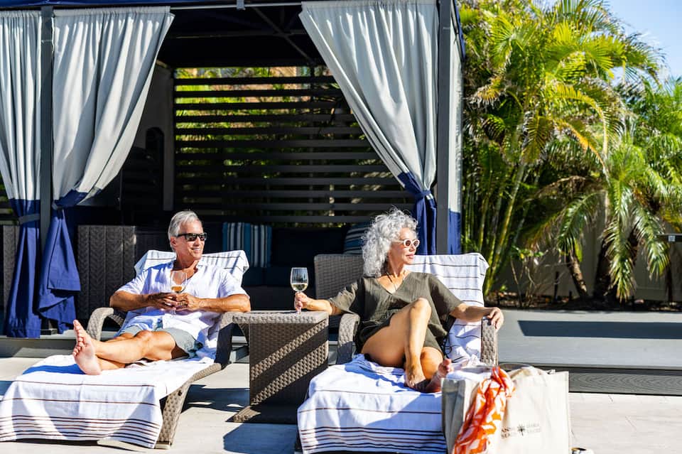 Couple relaxing on lounge chairs under cabana with ocean view and palm trees