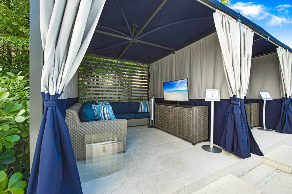 Covered outdoor lounge area with navy canopy, white curtains, wicker seating, and flat-screen TV