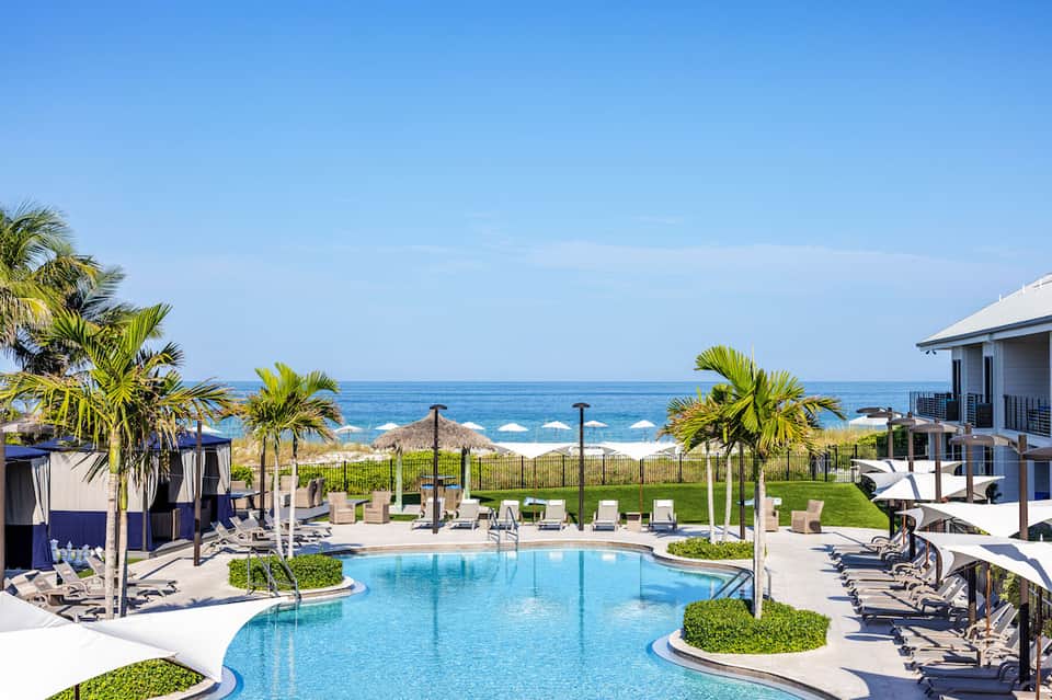 Luxury resort pool with ocean view, palm trees, lounge chairs, and beachfront landscaping