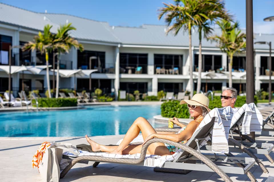 Guests relaxing on lounge chairs by pool with modern hotel building and palm trees