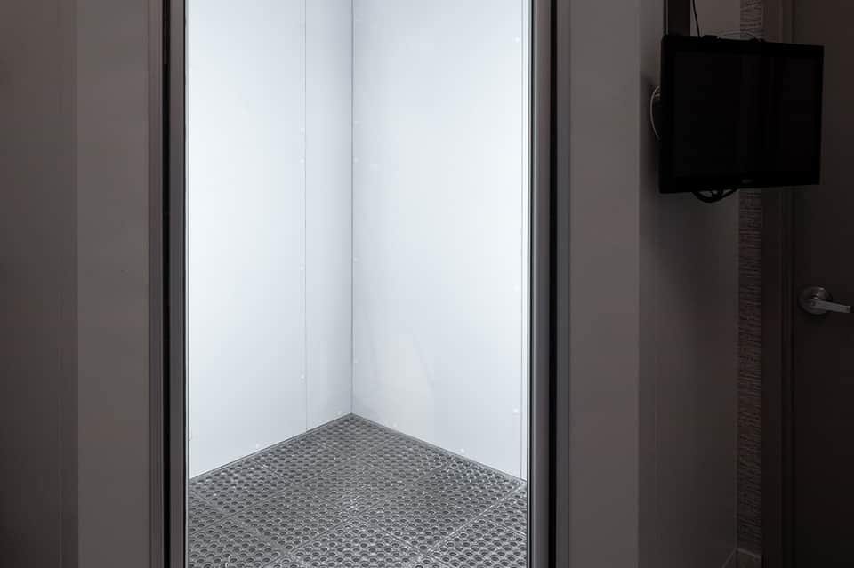 Clean, modern bathroom shower stall with white walls, glass enclosure, and textured floor mat