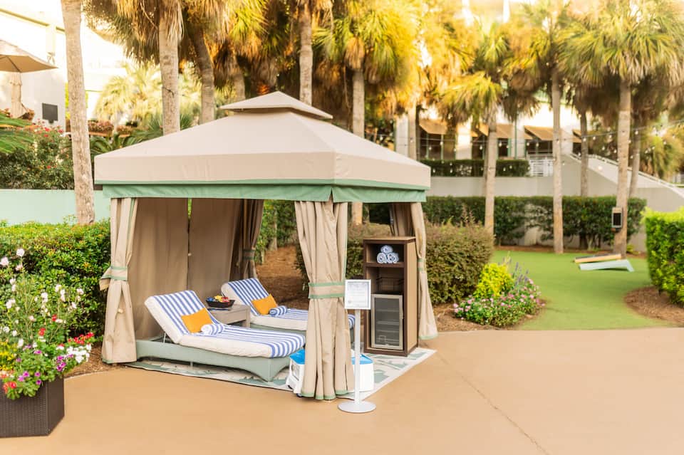 Outdoor cabana with striped loungers, palm trees, and landscaped gardens at a resort