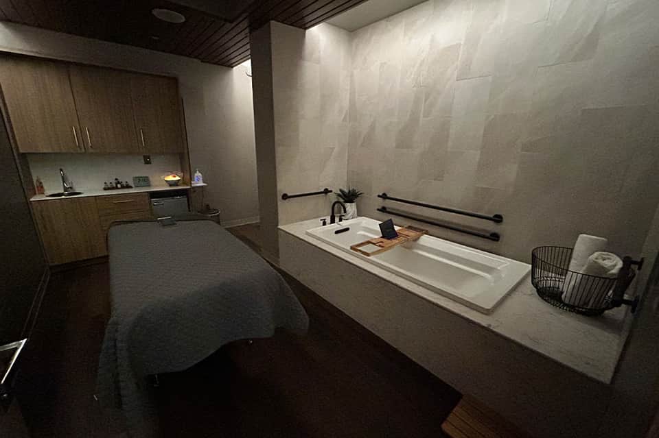 Modern minimalist bathroom with concrete walls, white bathtub, and integrated kitchen area