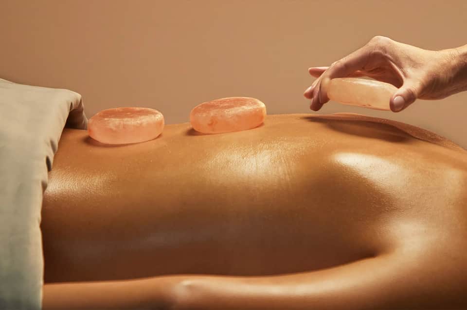 Spa therapist performing hot stone massage treatment on client's back