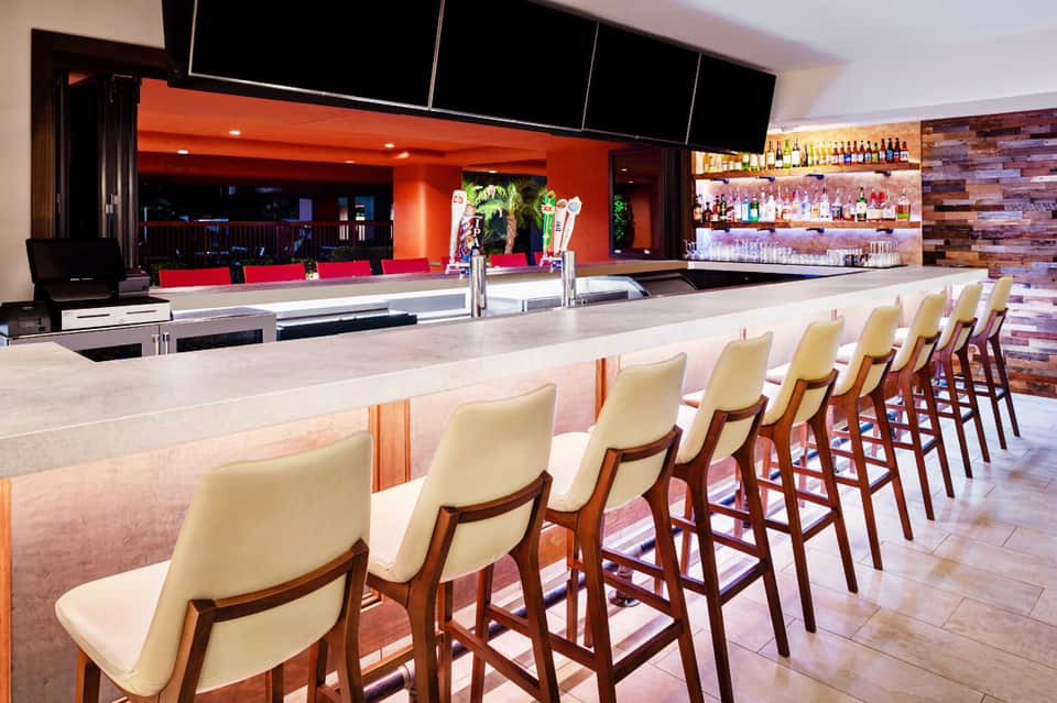 Modern bar interior with cream bar stools, orange accent walls, and well-stocked liquor shelves