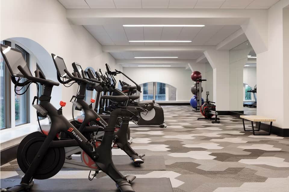 Bright fitness center with row of stationary bikes, exercise equipment, and geometric floor pattern