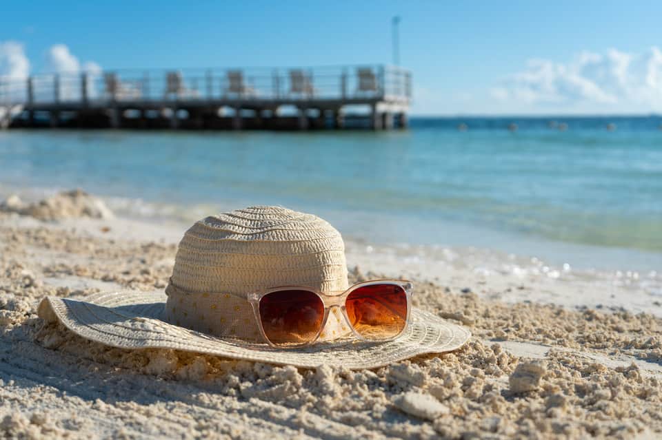 Straw hat and sunglasses on sandy beach with pier and ocean in background