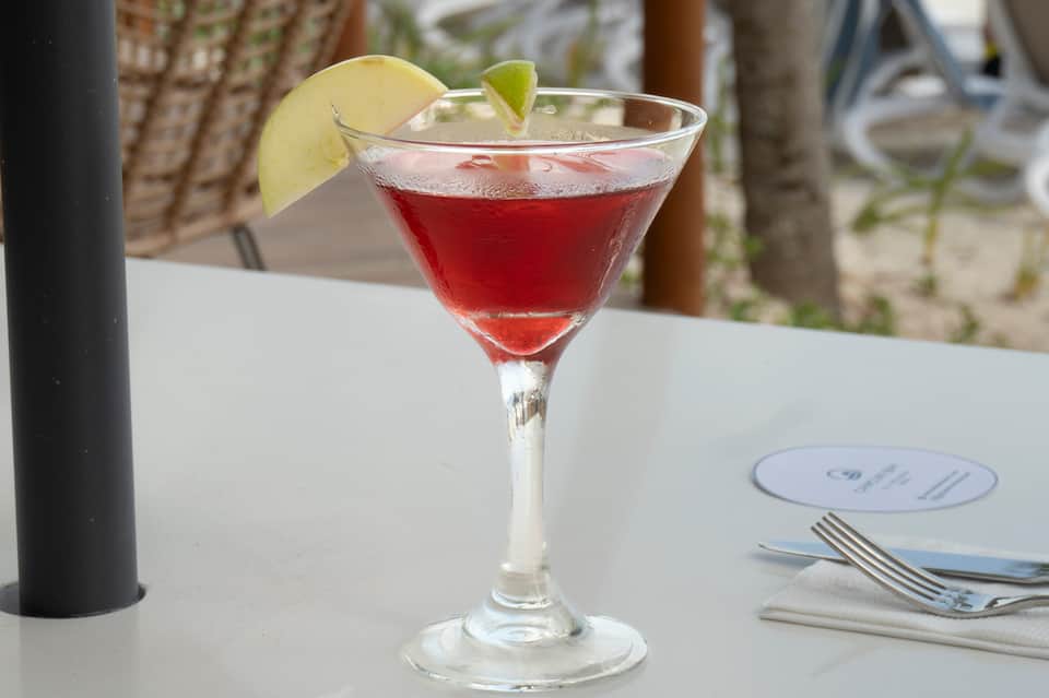 Red cocktail with lime garnish on white table at beachfront dining venue