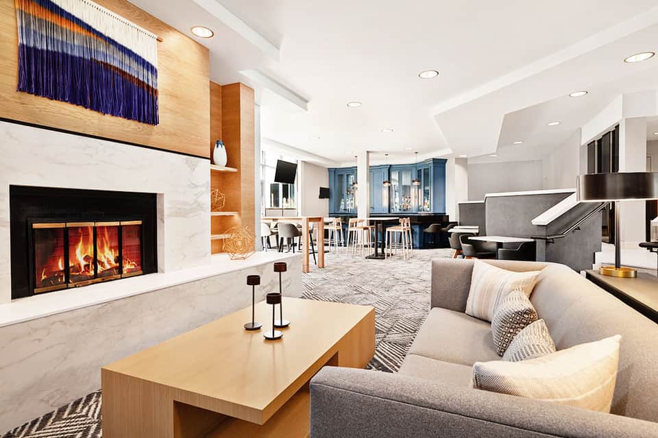 Modern hotel lounge with fireplace, grey seating, wooden accents, and grand piano