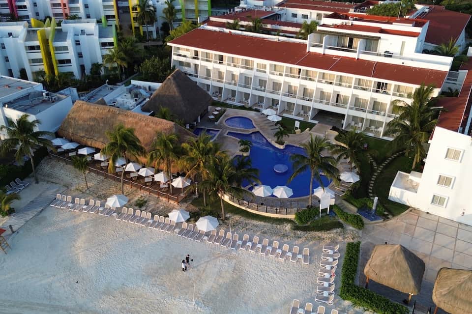 Aerial view of beachfront resort with pool, palm trees, lounge chairs, and sandy beach access