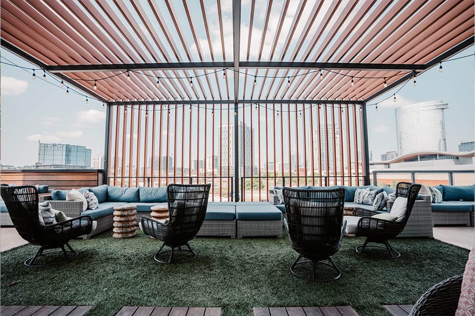 Modern rooftop lounge with retractable shade, blue seating, and city skyline views