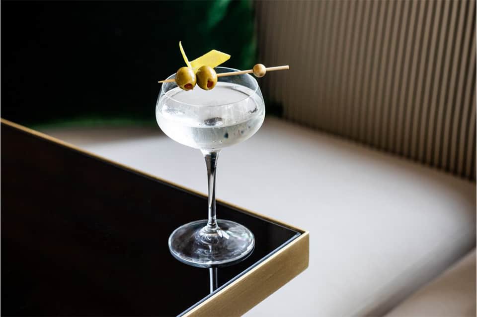 Cocktail glass with olives and lemon garnish on a bar counter