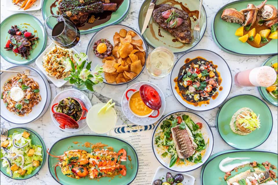 Overhead view of shared dining table with colorful plates of gourmet dishes, meats, seafood, and appetizers