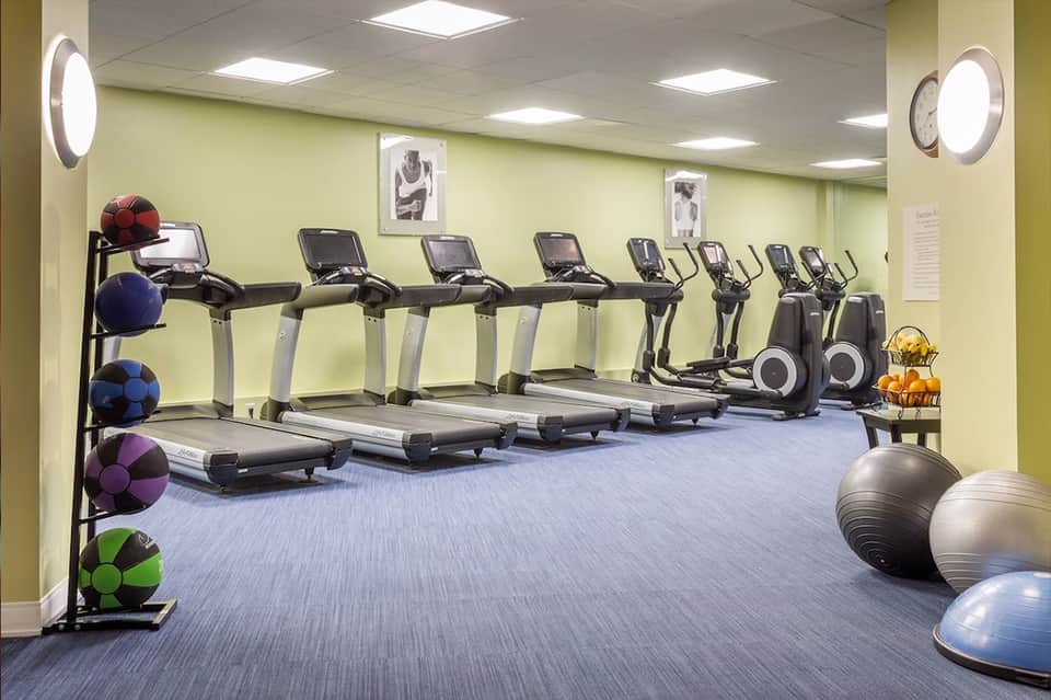 Modern gym with treadmills, ellipticals, exercise balls, and bright yellow-green walls