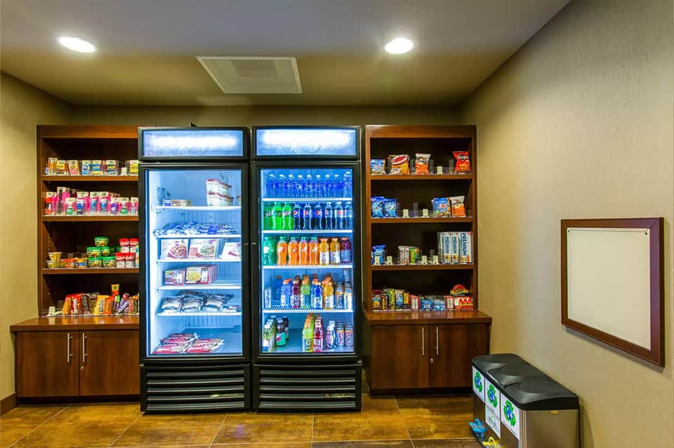 Hotel snack bar with refrigerated beverage cases, shelving with packaged goods, and wooden cabinetry