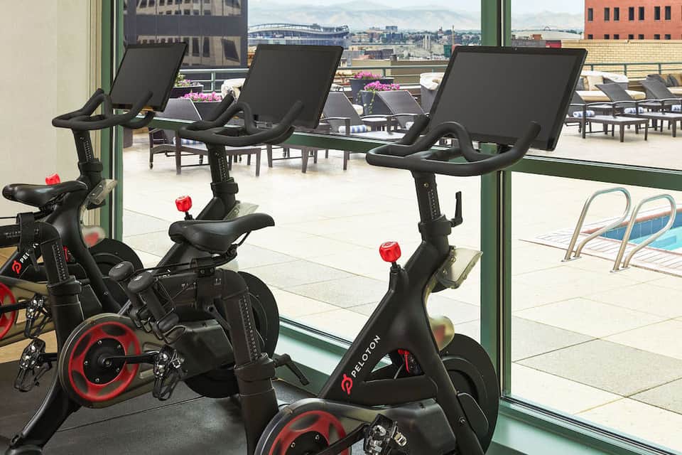 Fitness center with stationary bikes overlooking urban skyline and outdoor pool area through large windows