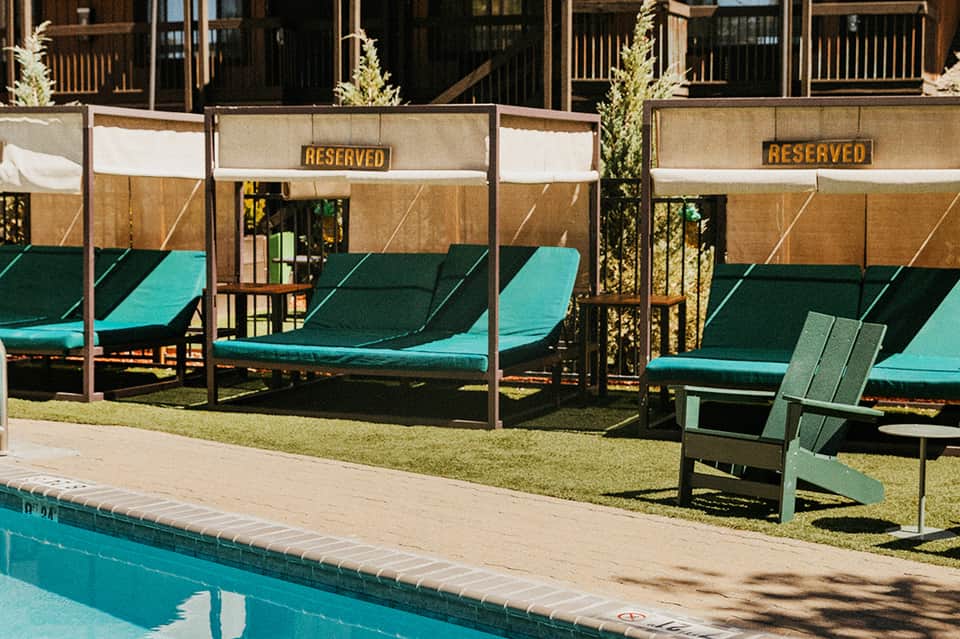Reserved cabana lounge chairs with turquoise cushions and shade canopies beside an outdoor pool