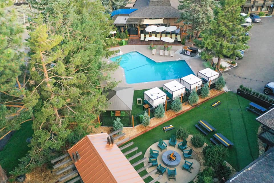 Aerial view of resort pool area with fire pit seating, cabanas, and surrounding pine trees